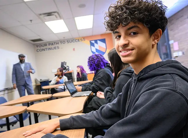 Young male student sitting in class with the professor giving a lecture in the background