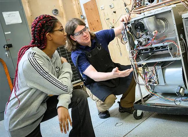 Two students working under the hood of a car in our automotive lab